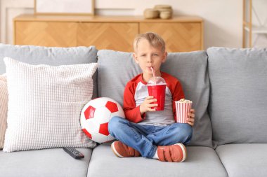 Evde futbol topu, patlamış mısır ve içkiyle kanepede oturan tatlı küçük çocuk.