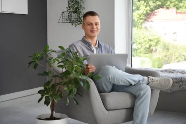 Modern yurt ofisindeki koltukta oturan dizüstü bilgisayarı olan genç bir serbest çalışan.