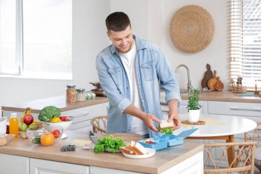 Genç adam mutfaktaki beslenme çantasına lezzetli bir sandviç koyuyor.