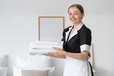 Otel odasında bir yığın temiz havlusu olan güzel oda hizmetçisi.