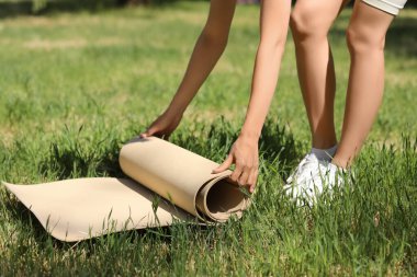 Genç bir kadın parkta yeşil çimlere yoga minderi yerleştiriyor.