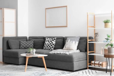 İçinde siyah kanepe, sehpa, saksı ve raf ünitesi olan güzel bir oturma odası.