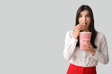 Gri arka planda patlamış mısır yiyen genç bir kadın.