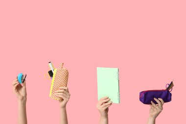 Not defteri, kalem kılıfı ve pembe arka planda kırtasiye malzemesi tutan kadın eller.