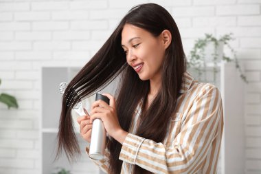 Güzel, genç, mutlu bir kadın evde saç spreyi sıkıyor.