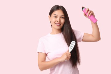 Pembe arka planda saç spreyi kullanan güzel, genç ve mutlu bir kadın.