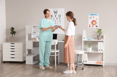 Kadın göz doktoru klinikteki hastaya deney çerçevesi veriyor.