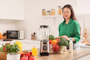 Mutfaktaki masada taze sebze ve blender ile genç Asyalı kadın.