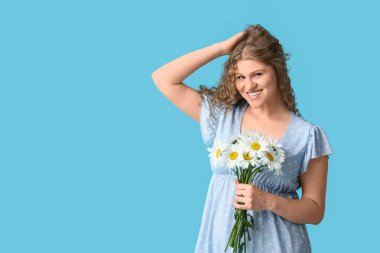 Mavi arka planda bir buket papatya çiçeğiyle güzel genç bir kadın.