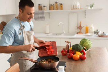 Genç adam mutfakta tavaya dolma biber koyuyor.