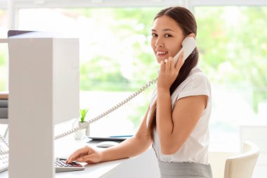 İş yerindeki genç bayan resepsiyonist telefonla konuşuyor.