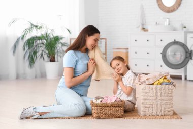 Gülümseyen anne ve kız temiz çamaşırlarla yerde oturuyor ve evdeki yumuşak havluya dokunuyorlar.