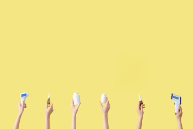 Termometreli eller, burun spreyleri ve sarı arka planda haplar.