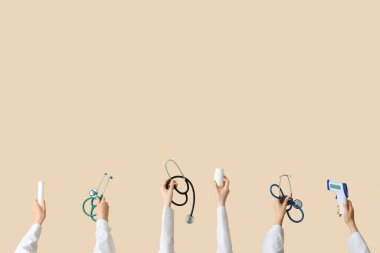 Bej arka planda steteskoplu, haplı ve termometresi olan kadın eller.