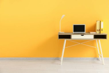 Ofiste sarı duvarın yanında dizüstü bilgisayarı ve lambası olan işyeri
