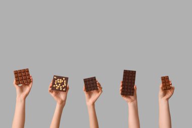 Gri arka planda farklı tatlı çikolataları olan kadın elleri.