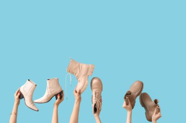 Mavi arka planda farklı çizmeler tutan kadın eller.