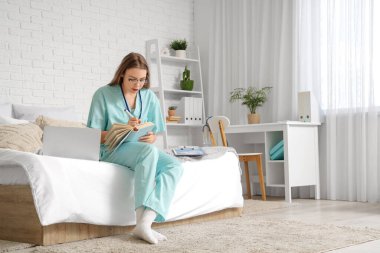 Modern dizüstü bilgisayar ve not defteriyle evde ders çalışan bir tıp öğrencisi.