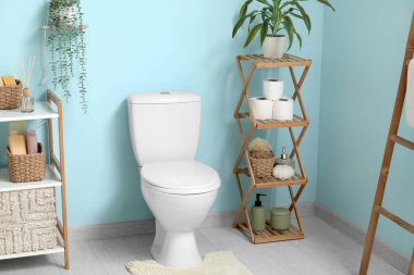 Seramik klozet, ev bitkisi, malzeme ve mavi duvarın yanında raf ünitesi olan şık bir tuvalet.