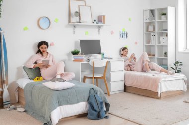 Yurt odasındaki yataklarda alet kullanan kız öğrenciler.