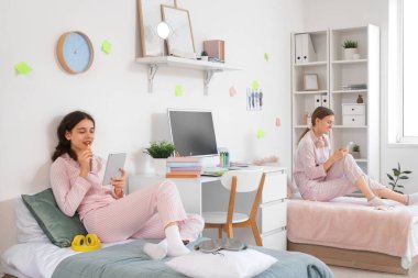 Yurt odasındaki yataklarda alet kullanan kız öğrenciler.