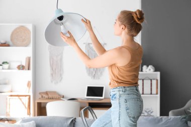 Merdivendeki genç kadın evdeki lambaya ampul takıyor.