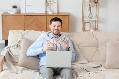 Bilgisayarlı genç erkek öğretmen evdeki kanepede online ders veriyor.