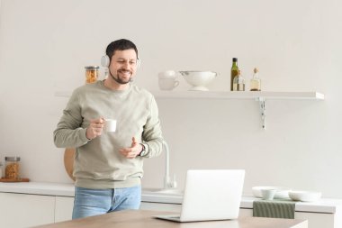 Dizüstü bilgisayarı ve kahvesi olan genç bir erkek öğretmen evde online ders veriyor.