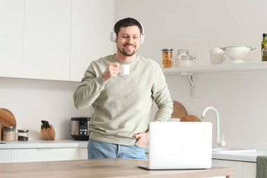 Dizüstü bilgisayarı ve kahvesi olan genç bir erkek öğretmen evde online ders veriyor.