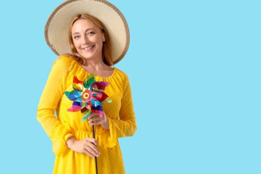 Mavi arka planda oyuncak yel değirmeni olan şapkalı olgun bir kadın.