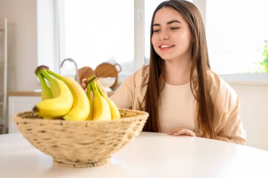 Genç bir kadın mutfaktaki masadan muz alıyor.