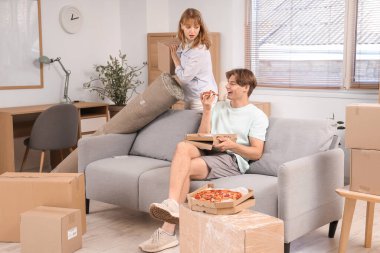 Genç adam, taşınma gününde oturma odasında elinde lezzetli pizzayla karton kutu ve kız arkadaşını tutuyor.