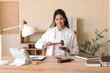 Female African-American lawyer with judge's gavel at table in office clipart