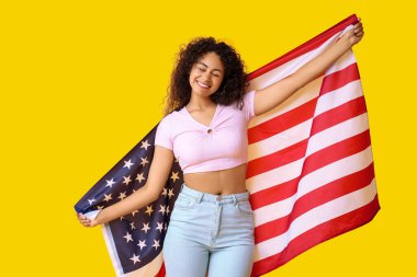 Sarı arka planda Amerikan bayrağı olan genç Afro-Amerikalı kadın.
