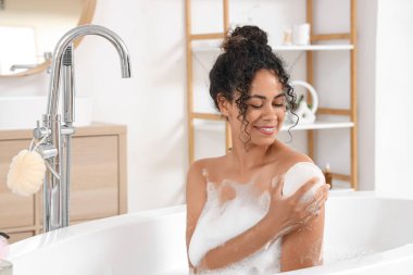 Güzel, genç, mutlu, Afro-Amerikan bir kadın evde sünger ve sabun köpüğüyle banyo yapıyor.