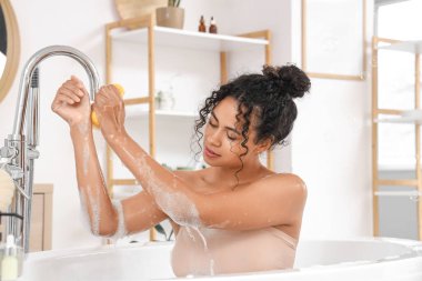 Güzel bir Afro-Amerikalı kadın evde sünger ve sabun köpüğüyle banyo yapıyor.