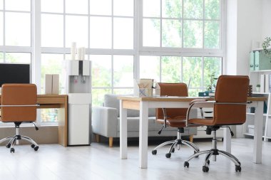 Masaları, kanepesi ve su soğutucusuyla aydınlık ofisin içinde.