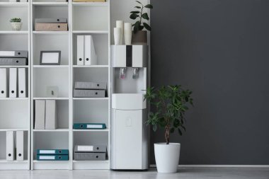 Kağıt bardaklı ve raflı modern su soğutucusu.