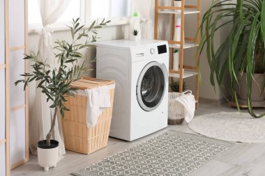 Çamaşır sepetleri, çamaşır makinesi ve pencerenin yanındaki ev bitkisi.