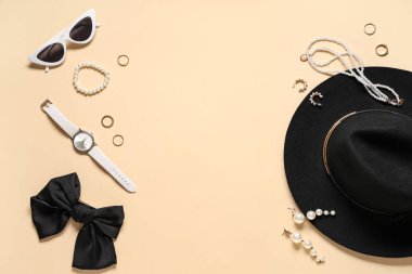 Bej arka planda şapka, fiyonk ve kol saati olan şık aksesuarlar. Üst görünüm