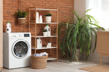 Çamaşır makinesi, sepeti ve raf ünitesi olan çamaşır odasının içi.