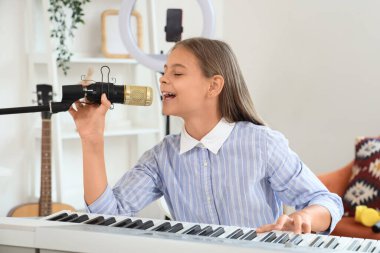 Evde sentezleyici ve mikrofon şakıyan küçük kız.
