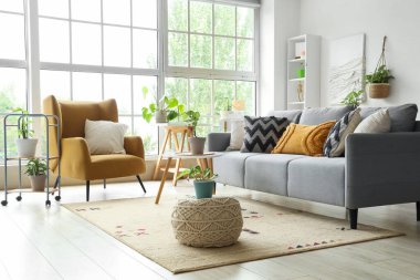 Yeşil bitkilerle, kanepeyle ve koltukla aydınlık oturma odasının içinde.