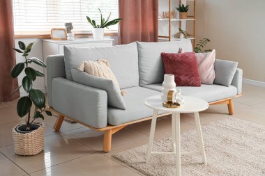 Oturma odasının içinde kanepede, masada ve penceresinde perdeler var.