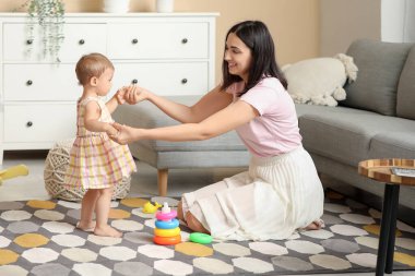 Küçük kız annesiyle evde yürümeyi öğreniyor.