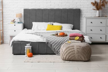 Yatak odasının içinde sonbahar dekorasyonu ve puf kazak var.