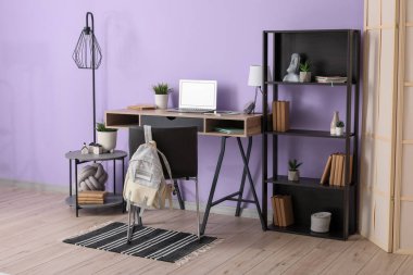 Mor duvarın yanındaki odada kırtasiye ve dizüstü bilgisayarı olan modern okul masası.