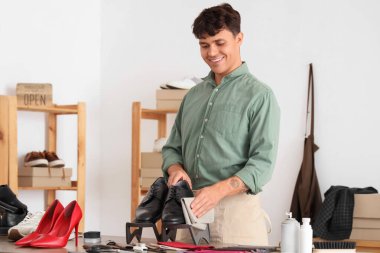 Male shoemaker cleaning shoes in repair shop clipart