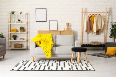 Modern oturma odası, şık gri kanepe, tabure ve sarı ekose örgü.