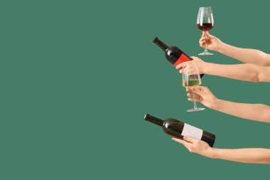 Yeşil arka planda kadehleri ve şarap şişelerini tutan kadın eller.